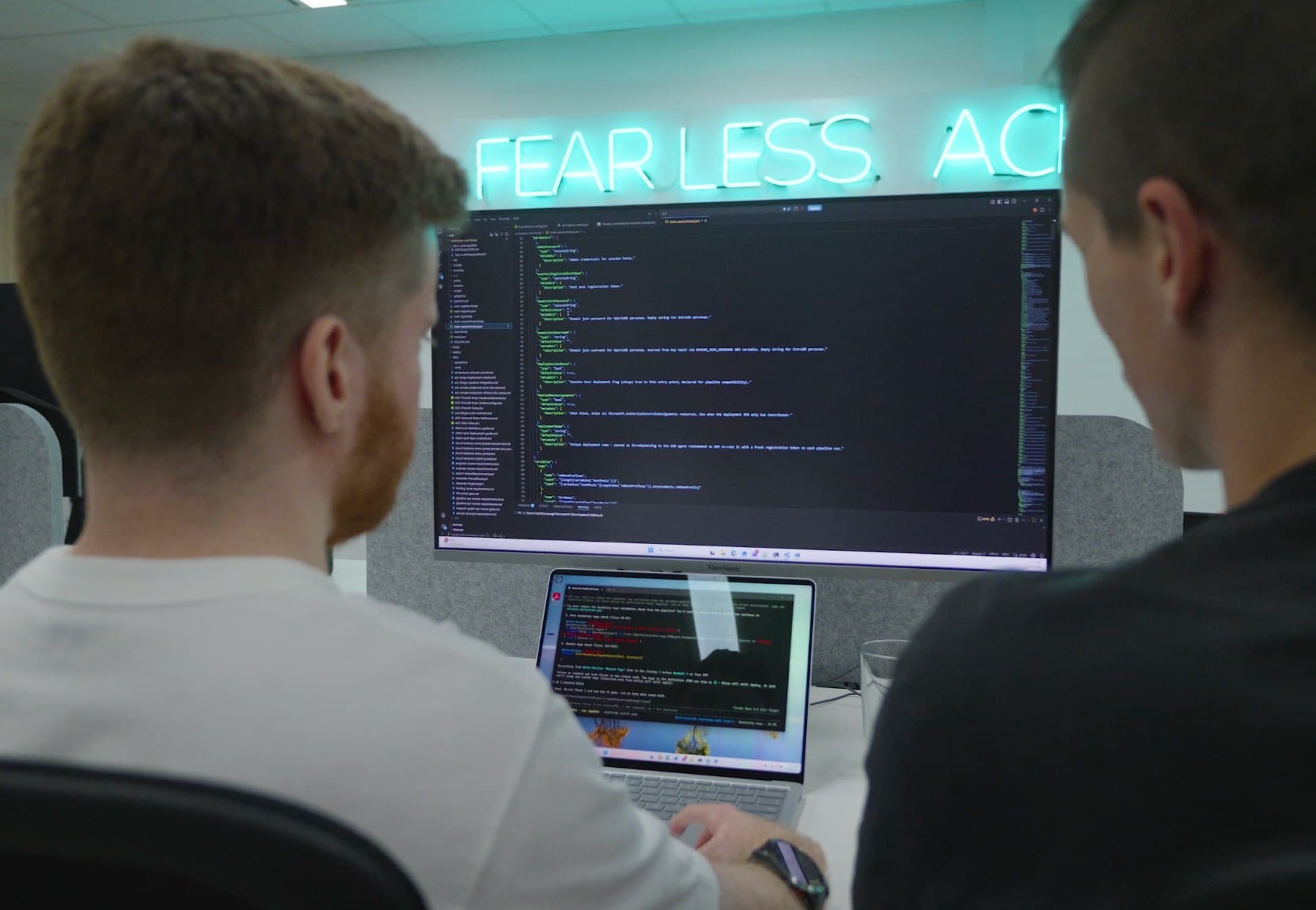 Two LAB3 engineers reviewing security code on a large monitor beneath a neon sign.