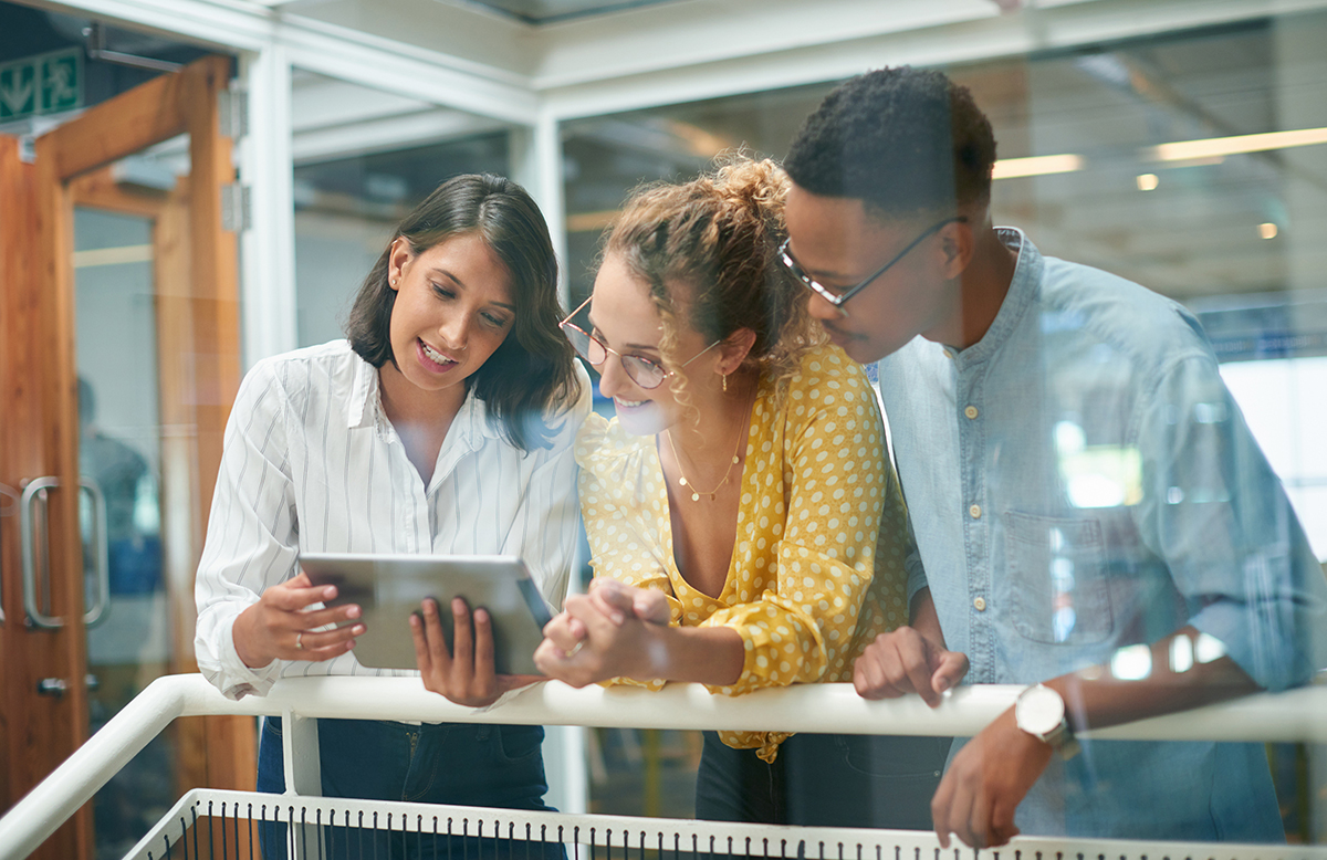 Three colleagues looking at a tablet together in a bright modern office